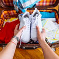 A person's hands putting sneakers into a suitcase. 