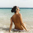 Rear view of shirtless woman sunbathing at a beach.