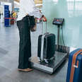 Woman putting suitcase on weights in airport measuring luggage.