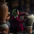 woman with headscarf crafting pottery vessel in darkness